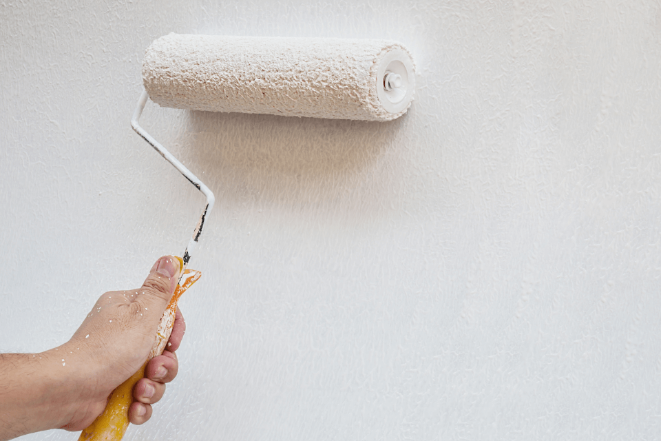 A person using a roller to apply Benjamin Moore primer on a wall, creating a smooth and even finish.